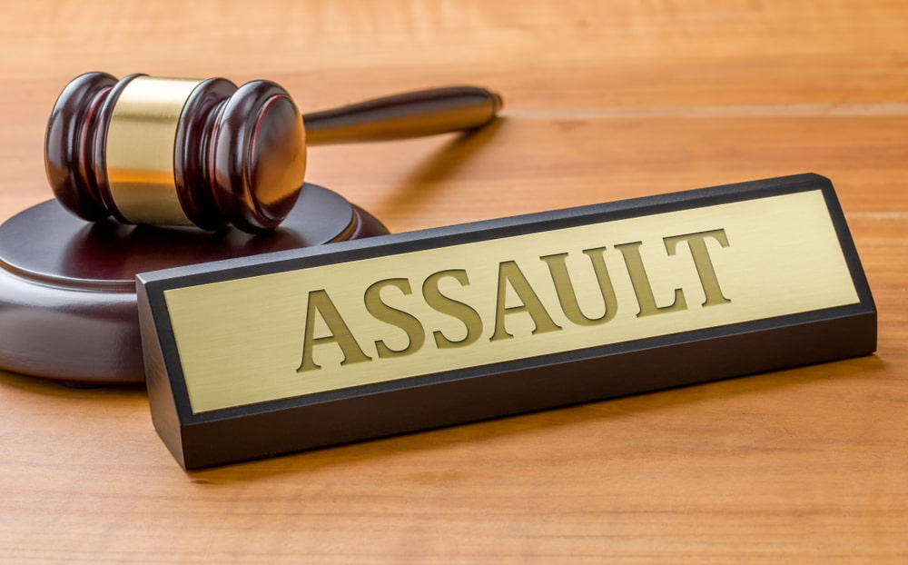 'assault' engraved on nameplate propped up against a judge's gavel on desktop