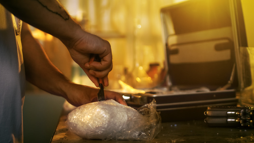 man cutting into a package of illegal drugs