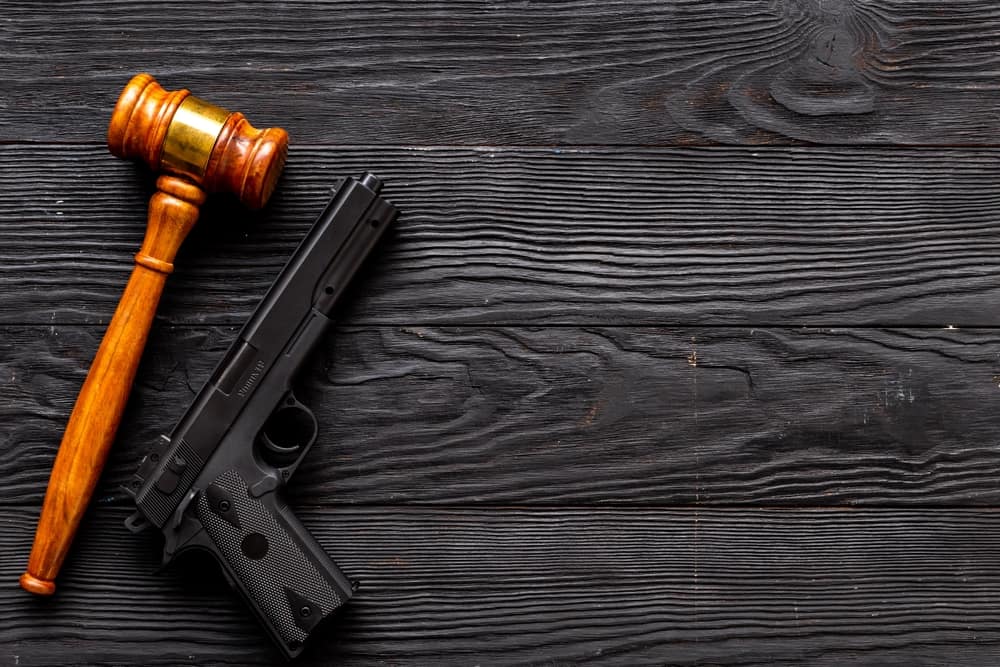 flat lay of judge's gavel next to a black gun on wooden tabletop