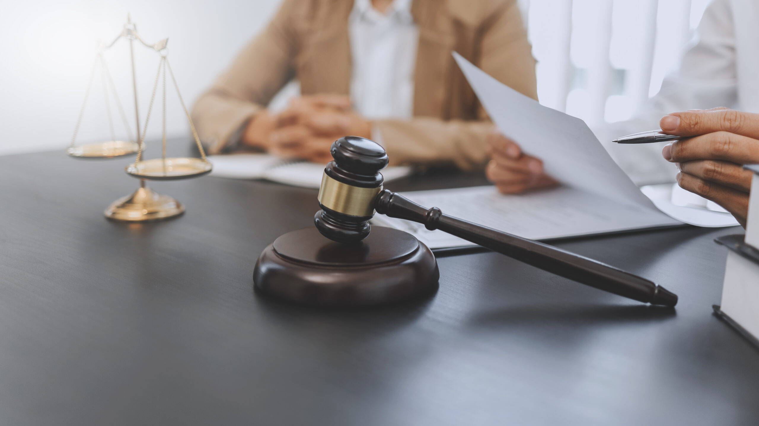 lawyer sitting at desk holding papers and client with hands folded next to him and judge's gavel propped up