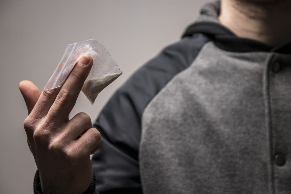 Mysterious faceless drug dealer holding a bag of cocaine or heroin.