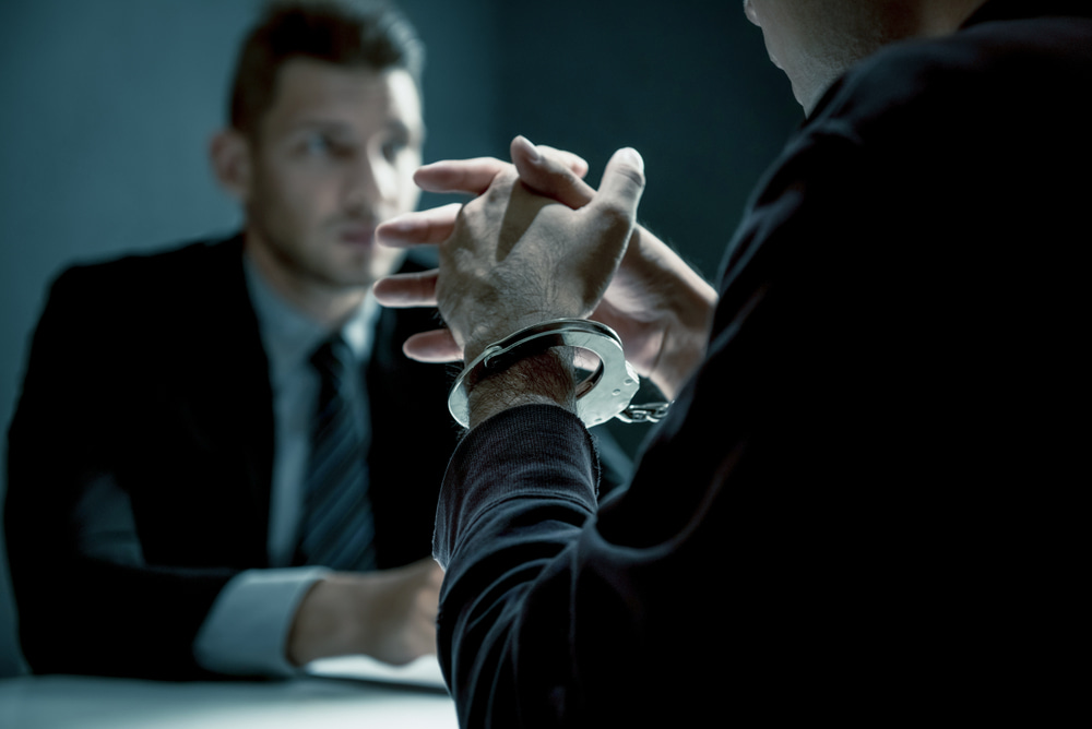 man in suit talking with detained individual wearing handcuffs