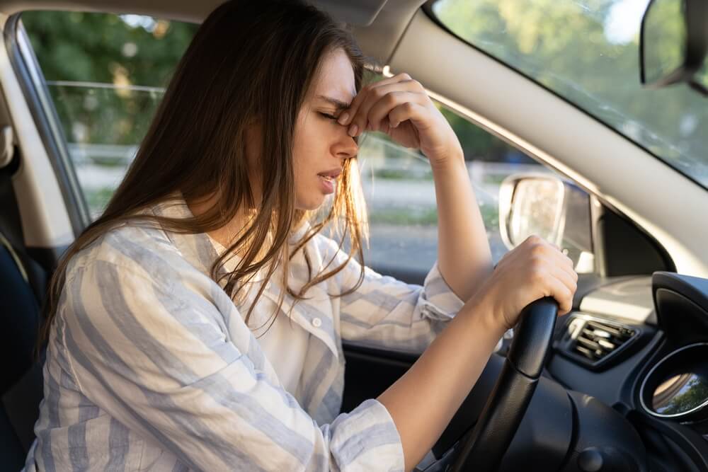 Tired young woman car driver suffering from headache migraine driving vehicle sit at driver seat touch painful forehead.