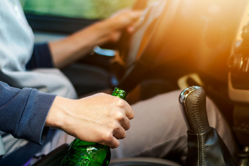 Drinking and driving, man holding alcohol bottle drinking alcohol while driving a car.