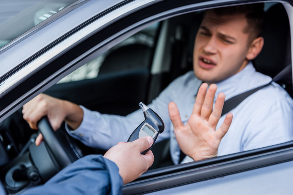 male driver holding his hand up to refuse a breathalyzer test held by a police officer's outstretched hand