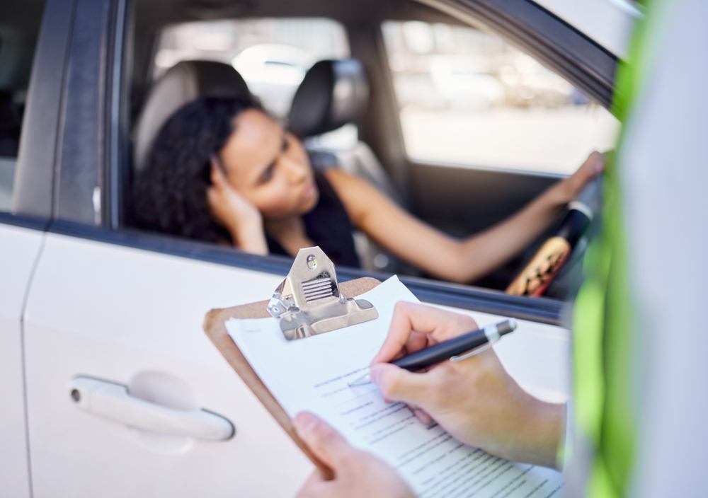 woman sitting in her car as law enforcement writes a traffic ticket